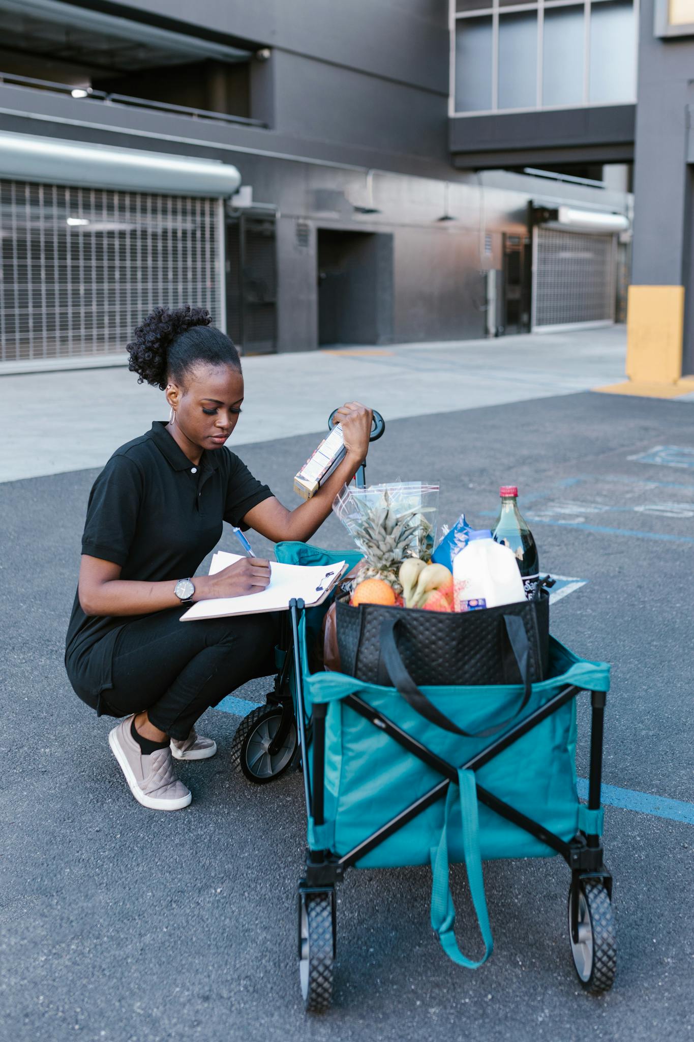 Woman checking off groceries from a clipboard beside a cart in a parking lot.